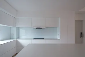 Modern kitchen with sleek, white countertops and transparent backsplash.