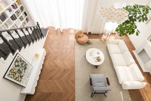 A modern living room with wooden flooring, a white sofa, minimalist furniture, and a large window with sheer curtains.