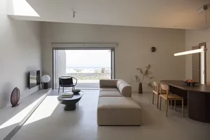 Modern minimalistic living room with concrete flooring, a white couch, and a large window overlooking an ocean view.