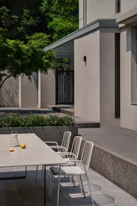 Outdoor dining area with a modern bistro set made of concrete, featuring a table and chairs under a sheltered pergola surroun