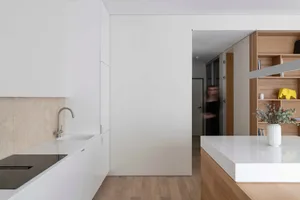 Modern residential kitchen with minimalist design, featuring white countertops and cabinetry, illuminated by natural light.