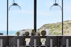 A modern dining room with glass vases and furniture overlooking a scenic landscape.