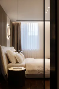 A minimalist bedroom with a white bed, transparent curtains, and a hanging lamp.