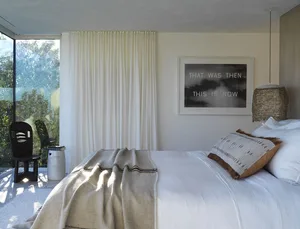 A minimalist bedroom with a white blanket and a frame that says 'That was then. This is now'.