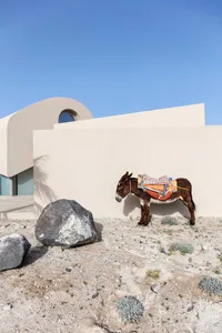 A minimalist house in a desert setting with a rock in the foreground, featuring sandstone walls and a circular window.