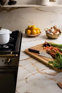 A modern kitchen with a marble countertop featuring a cutting board, knife, and various vegetables.