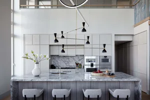 An elegant, modern kitchen with a marble countertop and industrial lighting fixture above a white kitchen island with seating