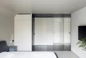 A modern minimalist bedroom with white walls, a black headboard bed, and a minimalistic design.