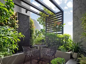 Modern outdoor patio with metal chairs, concrete planters filled with lush green plants, and a black lattice wall.