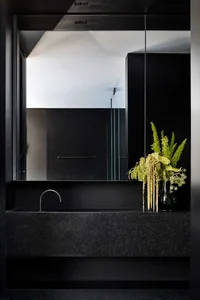 A modern bathroom with black granite countertops, a large mirror, and a vase of flowers.