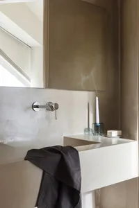 Modern minimalist bathroom featuring concrete walls and a floating vanity with a wall-mounted faucet and a lit candle.