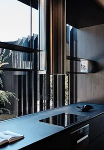 A modern kitchen with glass cabinets, dark wooden walls, and a large window.