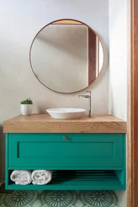 Modern bathroom with turquoise wooden cabinet, wooden countertop, sink, and round mirror.