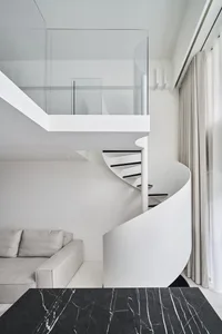 A modern residential interior featuring a spiral staircase with glass railings and white walls.