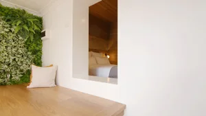 A minimalist bedroom with a vertical garden wall and a window cut-out revealing a cozy bed.