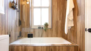 A modern bathroom with wood paneling, a glass-enclosed bathtub, and a window