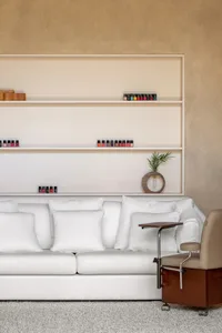 A modern beauty salon interior featuring a white couch with white cushions, a white upholstered cabinet, and a white wall wit