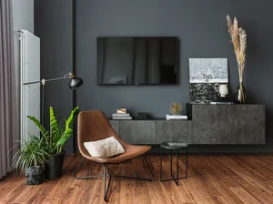 A modern living room with dark gray walls, concrete furniture, and a brown woven chair with a fluffy pillow.