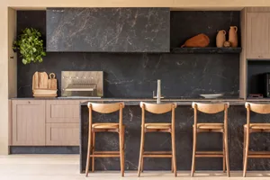 Modern kitchen with minimalist design, featuring black marble countertops and backsplash, and wooden stools at the island.