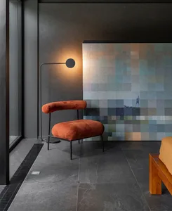 A modern living space featuring an orange velvet armchair with a metal frame, illuminated by a floor lamp in a dark room with