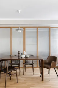 A modern minimalist dining room with wooden furniture and frosted glass partitions.