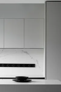 A modern minimalist kitchen with white cabinets and black accents, featuring a quartzite countertop and backsplash.