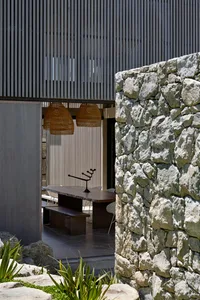 A modern residential dining area with a large wooden dining table, wicker pendant lights, and stone walls.