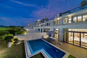 Modern residential building with concrete walls and glass windows, featuring a swimming pool and outdoor dining area.