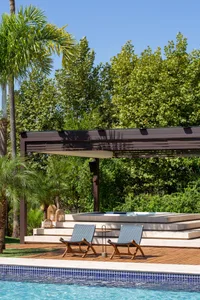 Two blue lounge chairs under a brown pergola with a rectangular pool in the foreground.