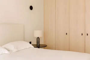 Minimalist bedroom featuring wooden cabinets and a bed with white linens.