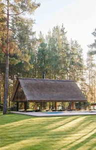 A minimalist residential house with a thatched roof surrounded by trees.