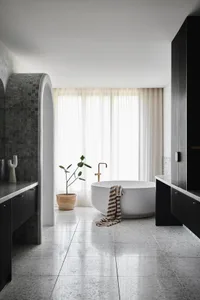 Modern, minimalist bathroom featuring a cement floor, white bathtub, natural light, and a single plant.