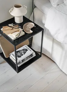 A minimalist bedroom featuring a black side table with a stack of books and a decorative vase.
