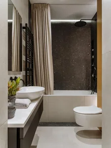 Modern bathroom featuring a white vanity with a sink, a bathtub with a dark stone wall, and a toilet.