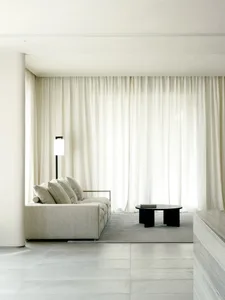 Minimalist living room with textured fabric sofa, sheer curtains, and round black table.