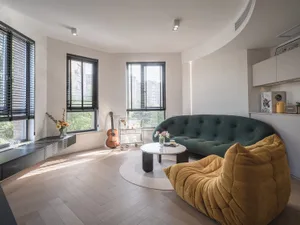 A modern living room featuring minimalist furniture, large windows, and a wooden floor with sunlight streaming through.