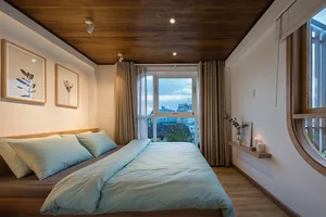 A modern bedroom with a wooden ceiling, fabric bedding, and a large window with curtains.