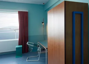 A minimalist living room featuring a wooden cabinet and blue curtains and floor.