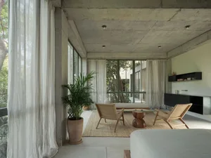 An elegant, minimalist residential space featuring a concrete ceiling, glass windows, and wooden furniture.
