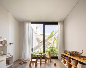 A modern children's playroom with a wooden table and chairs, toy storage, and a view of the garden through large windows.