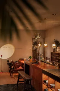 Modern kitchen with wooden countertops, cabinets, and dining table, featuring chairs, decorative items, and potted plants in a warm and inviting atmosphere