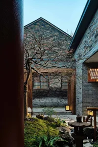 A stone building with a brick facade and a large tree in front, creating a sense of depth and connection between nature and architecture