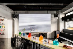 Modern design showroom with a large flat screen TV, chairs, and a dining table with decorative items, set in a stylish environment