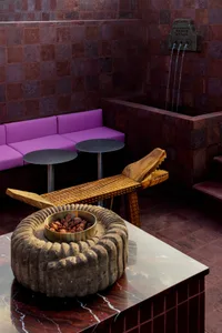 Cozy living area with a purple couch, chair, and dining table, featuring a vase and dim lighting