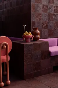 A modern living area with a purple couch, red chair, vases, and apples, creating a cozy and inviting atmosphere with bold colors and simple decorations