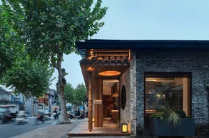 A stone building with a wooden doorway and stone arch, set in a busy urban environment with people and motorcycles
