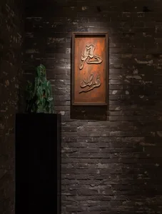 Elegant interior space with a black stone wall, wooden frame, decorative vase, and sculpture, reflecting artistic elements