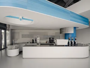 Industrial kitchen with a large white countertop, coffee makers, and scattered bottles, with a clean and organized atmosphere