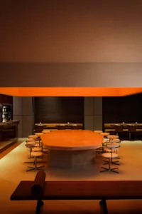 A modern restaurant interior with a large wooden dining table surrounded by chairs in a stylish setting