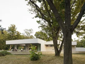一座現代建築，外觀為混凝土材質，搭配一棵大樹與戶外座位區，人們在此聚集社交